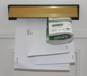 Paper letters have been posted through a gold letterbox on a white door.